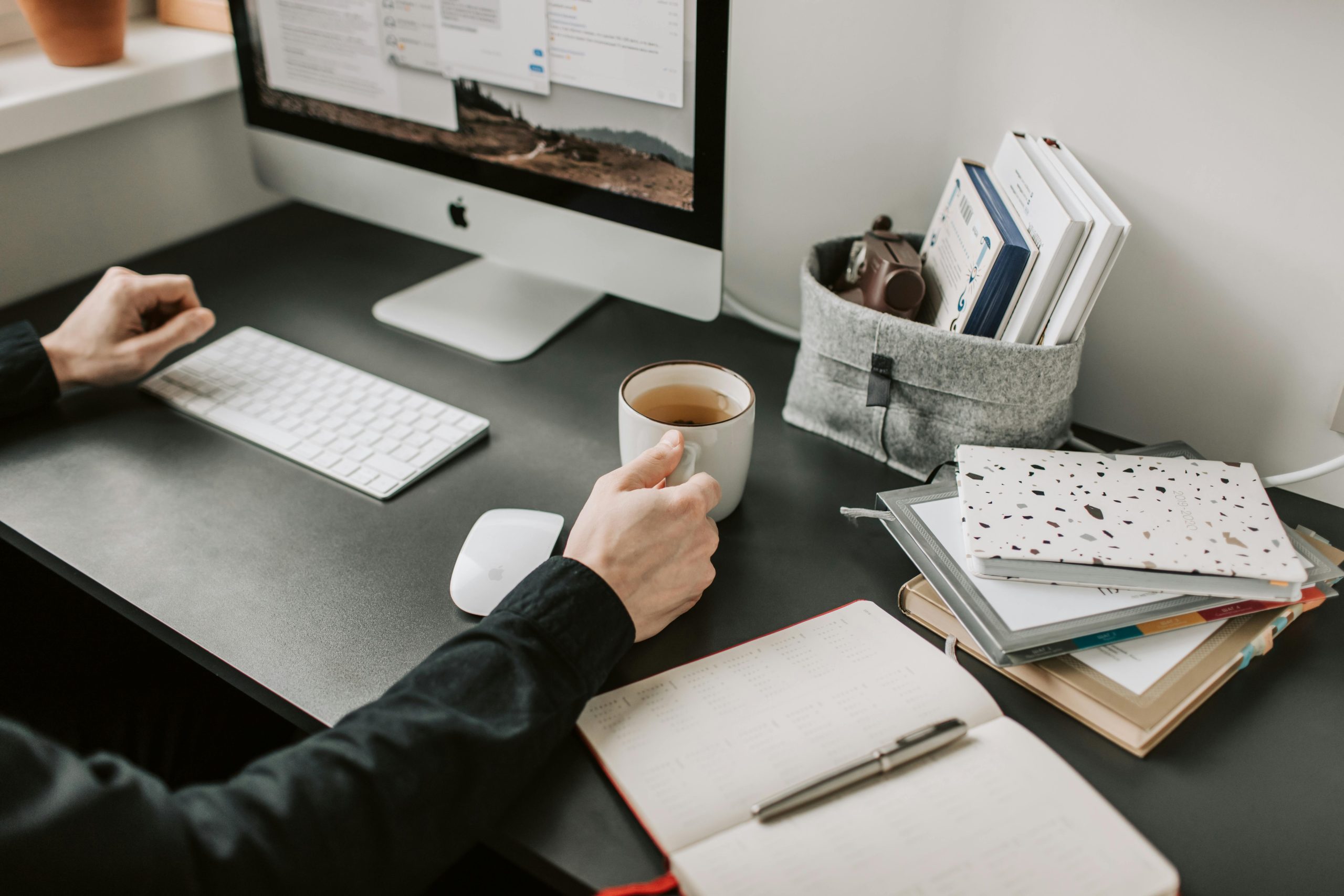 Man sipping coffee at a modern workspace with computer and notebooks.